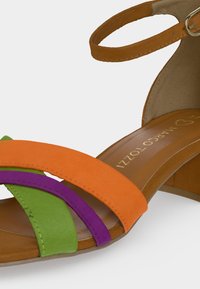 Sandale en cuir avec des lanières orange, vertes et violettes, boucle à la cheville et petit talon bloc en tons marron clair.