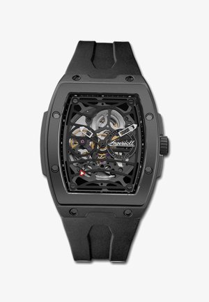 Black skeleton watch with a rectangular case, rubber strap, and visible automatic movement. Features metal accents and a red triangular detail.