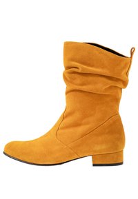 Bottines en daim jaune vif, avec un design drapé, un petit talon épais et une texture lisse. Détails de couture sur les côtés.