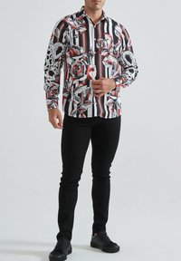 Chemise à boutons avec des rayures noir et blanc et des motifs floraux rouges. Manches longues, col, en tissu léger.