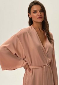 Jedwabny szlafrok w delikatnym odcieniu różu z głębokim dekoltem w kształcie V i szerokimi rękawami; posiada dopasowany pasek, gładką teksturę i minimalistyczny design.