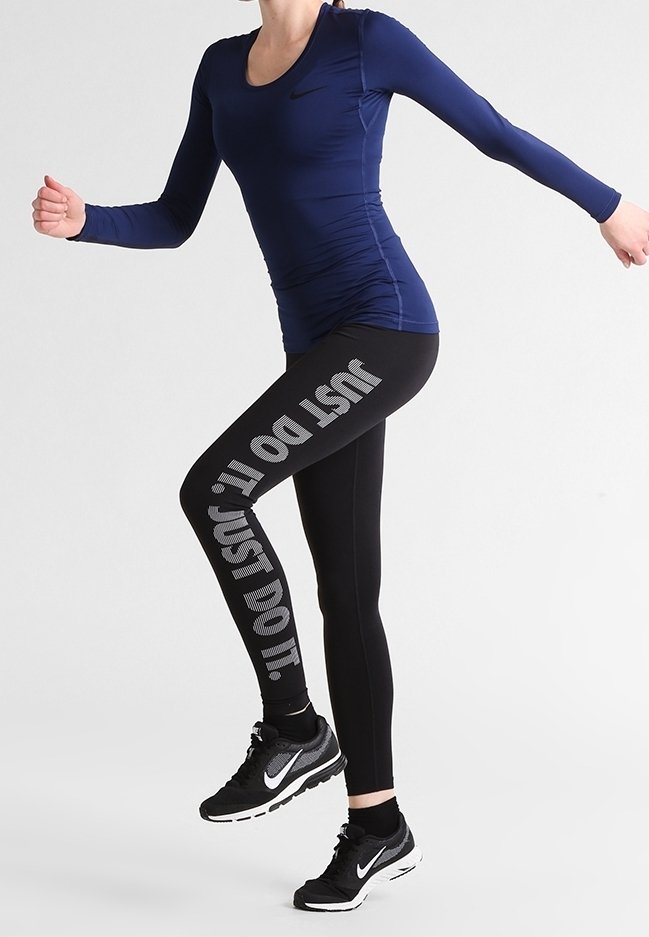 Langsleeve marineblauw top met een ronde hals, gecombineerd met zwarte leggings met een gedurfde grijze "JUST DO IT" grafiek. Zwarte hardloopschoenen met zilveren accenten.