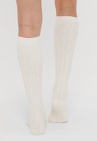 Knee-high white socks with a textured cable knit pattern and ribbed cuffs, made from a soft, lightweight material.