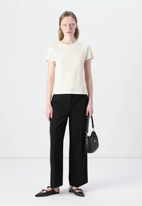 T-shirt corto crema con maniche corte, pantaloni neri a gamba larga e scarpe basse nere. La modella tiene una borsa nera. Outfit semplice e casual.