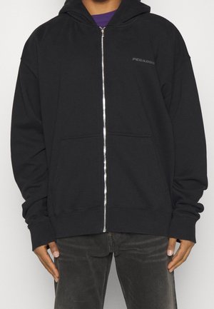 Schwarze Kapuzenjacke mit Reißverschluss aus weichem Stoff, ausgestattet mit einer Kapuze, Fronttaschen und einem kleinen Logo auf der Brust. Die Bündchen und der Saum sind gerippt.