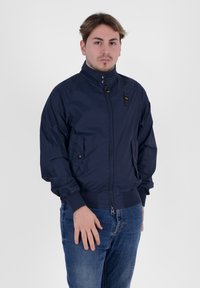 Giacca bomber marina con colletto alto, chiusura zip frontale, tasche laterali e polsini e orlo a coste. Tessuto liscio e leggero con dettagli minimi.