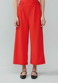 Rode wijde broek met een hoge taille, knoopaccenten op de tailleband en een zachte, gladde stof. Perfect passend voor een relaxte fit.