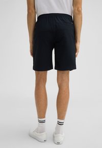 Marineblauwe shorts van een textuurstof, met een elastische tailleband en een zak aan de achterkant. Gecombineerd met witte schoenen en gestreepte sokken.