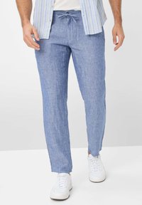 Pantaloni in lino azzurro chiaro con vita elasticizzata e cordoncino. Design slim fit con polsini, abbinati a sneakers bianche.