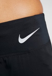Cinturilla deportiva negra con una textura suave y un prominente logo de swoosh blanco de Nike. La tela parece elástica y ajustada.