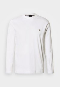 Fehér, hosszú ujjú póló sima pamutból, kerek nyakkivágással és egy kis fém logóval a bal mellrészen.