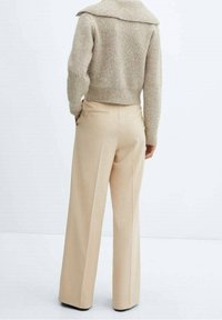 Beige wijde broek met een elegante pasvorm, voorzien van achterzakken en een gladde textuur, gecombineerd met een licht, geribbeld sweater.