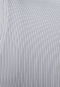Tecido branco com nervuras e linhas verticais estreitas, com uma textura suave, exibindo um design sem emendas e detalhes de costura subtil.