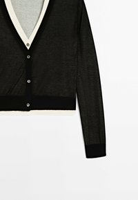 Cardigan transparent noir à manches longues avec bordure blanche, encolure en V et quatre boutons à l'avant, présenté à plat sur un fond blanc.