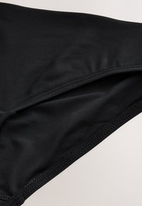 Primo piano di tessuto nero con cuciture visibili e dettagli della cucitura su una superficie tessile liscia.