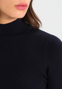 Navy-randig polotröja tillverkad av mjuk tyg, med hög krage och texturerad mönster över hela.