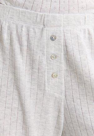 Primer plano de unos pantalones de punto blancos con textura de rayas verticales y tres pequeños botones redondos en el panel frontal de la bragueta.