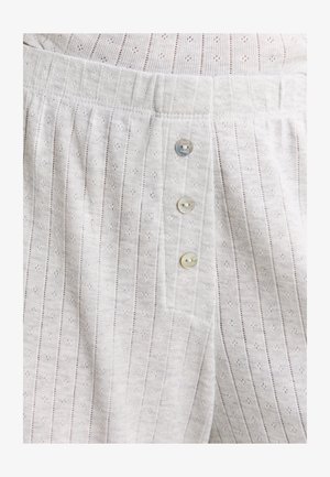 Primer plano de unos pantalones de punto blancos con textura de rayas verticales y tres pequeños botones redondos en el panel frontal de la bragueta.