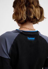 Zwarte en grijze sweatshirt met een geribbelde textuur, blauwe kraag en Hummel-logo op de achterkant van de nek. Heeft een geïsoleerd, sportief ontwerp.