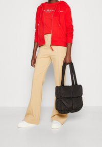 Hoodie en coton rouge, haut rouge, pantalon évasé beige et sac à main matelassé noir. Des baskets blanches complètent la tenue. Design simple et texture lisse.