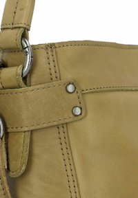 Sac à main en cuir khaki avec des détails en métal argenté, présentant une sangle cousue et des panneaux latéraux. Texture lisse avec un design minimaliste.