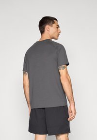 Grå atletisk T-shirt med korte ærmer, rund hals og en glat tekstur. Båret med sorte shorts, der viser et enkelt design og afslappet pasform.