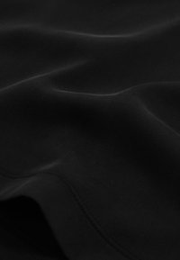 Tissu noir lisse avec des plis subtils et une couture visible traversant en diagonale la partie inférieure du tissu.