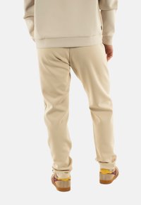 Pantalones de chándal beige hechos de una tela suave con un corte relajado, que presentan puños elásticos y se combinan con zapatillas de corte bajo multicolores.