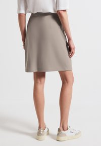 Beige polyester-hame, joka ulottuu keskikohtaan, jossa on sileä pinta ja piilotettu takavetoketju, yhdistettynä valkoisiin tennareihin.