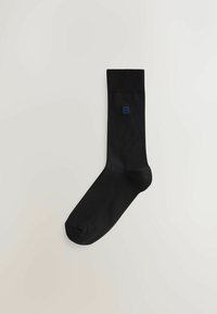 Calza nera in cotone misto; bordo a coste e texture liscia. Piccolo logo blu sul lato. Design semplice e lineare.