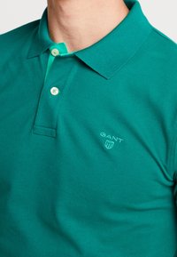 Turbkusowy polo z klasycznym kołnierzykiem, dwoma guzikami i dyskretnym haftem logo na piersi. Gładki materiał bawełniany.