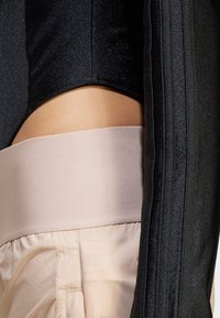 Svart strukturert stoff med en glitrende finish går over til en glatt, lys rosa midjebånd. Designet har et lagdelt, tettsittende utseende.