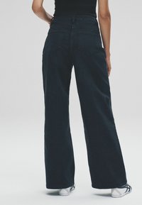 Džíny s širokým nohavicami, tmavomodré, s vysokým pásom, ktoré majú dve zadné vrecká a čistý dizajn. Tkanina sa zdá byť pevná s hladkou textúrou.