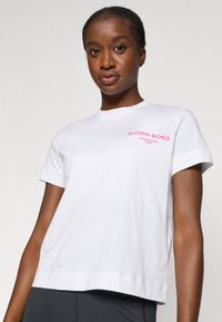 Valge puuvillane T-särk lühikeste varrukatega, millel on roosa "BJÖRN BORG STOCKHOLM 1956" kiri vasakul rinnal. Mugav lõige ja ümmargune kaelus.