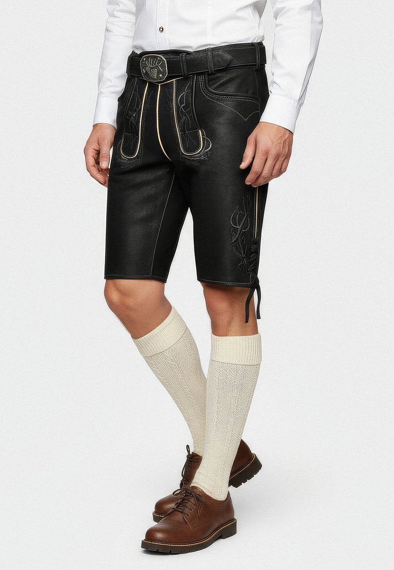 Pantalones cortos de cuero negro con costuras amarillas y acentos bordados, combinados con calcetines de color crema hasta la rodilla y zapatos marrones con cordones.