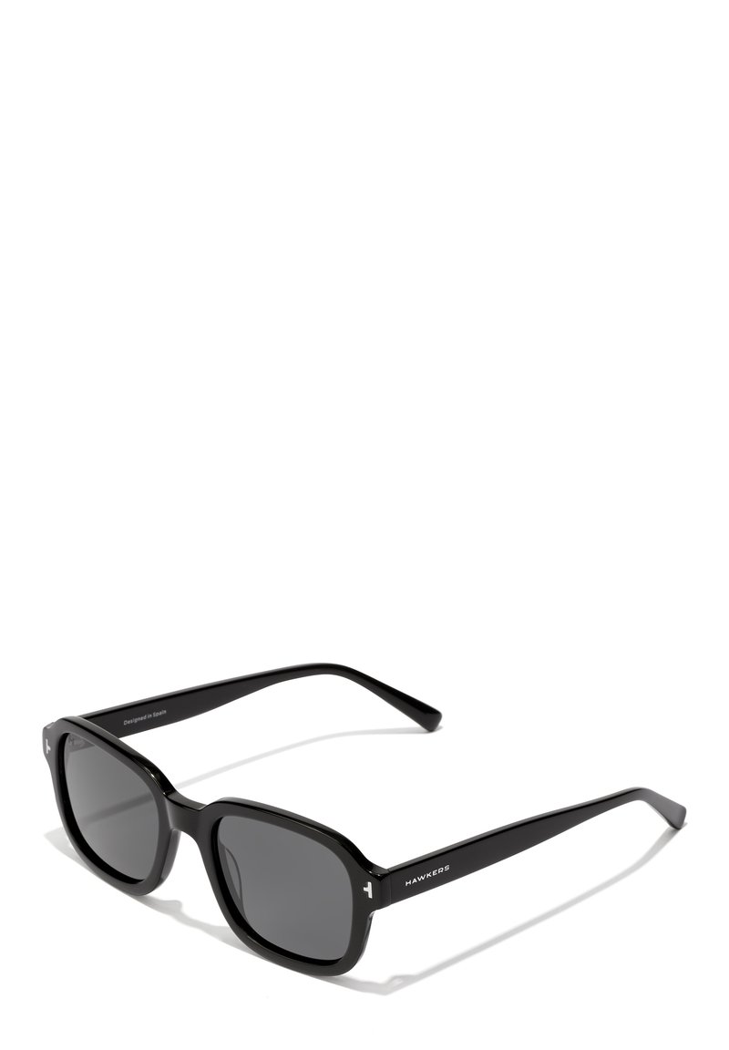 Črne sončne očala s kvadratno obliko, plastičnim okvirjem, temno sivo lečo in logotipom ob strani. Imajo elegantne ročke s sijajnim zaključkom.