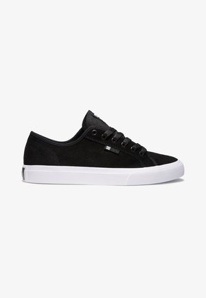 Black suede sneakers with a white rubber sole, round toe design, six eyelets, and textured accents for grip. DC logo on the side.