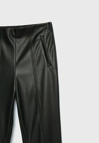 Zwarte nep-lederen broek met een gladde textuur, zijzak met rits en verticale zoomdetails voor een getailleerde pasvorm.