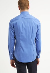 Košile s dlouhým rukávem a knoflíky světle modré barvy. Má přizpůsobený zadní díl s zakřiveným lemem a manžetami s jedním knoflíkem. Hladká textura.