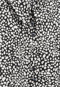 Tissu à motifs noir et blanc avec des formes irrégulières, doté de boutons sur le devant et d'un col, présentant une apparence texturée.