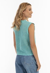 Top azzurro chiaro senza maniche con scollatura a onde e design traforato; abbinato a jeans in denim blu a vita alta.