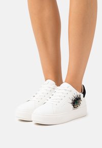 Vita lädersneakers med tjocka sulor, med ett dekorativt öga-motiv i svart, guld och turkos, samt svarta detaljer vid hälen.