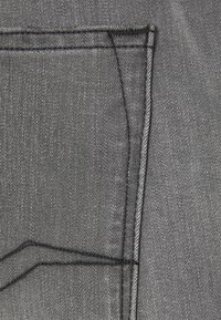 Tela de mezclilla gris con costuras visibles. Presenta un contorno de bolsillo parcialmente visible, con una textura suave y un ligero brillo.