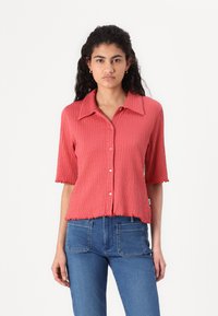 Korte mouwen, knoopsluiting shirt van geribd koraalstof. Heeft een puntige kraag, gegolfde zoom en een relaxte pasvorm. Gekocht met blauwe jeans.
