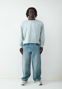 Jasnoniebieska koszula z długim rękawem w połączeniu z luźnymi, wyblakłymi niebieskimi dżinsami. Całość uzupełniają szare i białe trampki.