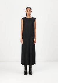 Rochie maxi neagră, fără mâneci, cu pliseuri verticale și decolteu rotund. Asortată cu cizme negre mulate. Textură netedă și siluetă fluidă.