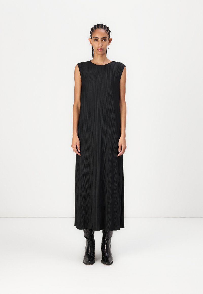 Rochie maxi neagră, fără mâneci, cu pliseuri verticale și decolteu rotund. Asortată cu cizme negre mulate. Textură netedă și siluetă fluidă.