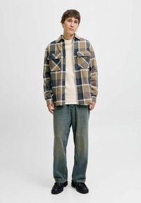 Rutet flannel skjorte i tan, brunt og marineblå; cremet sweater under; lyseblå jeans; sorte sko; tekstureret stof og afslappet pasform.