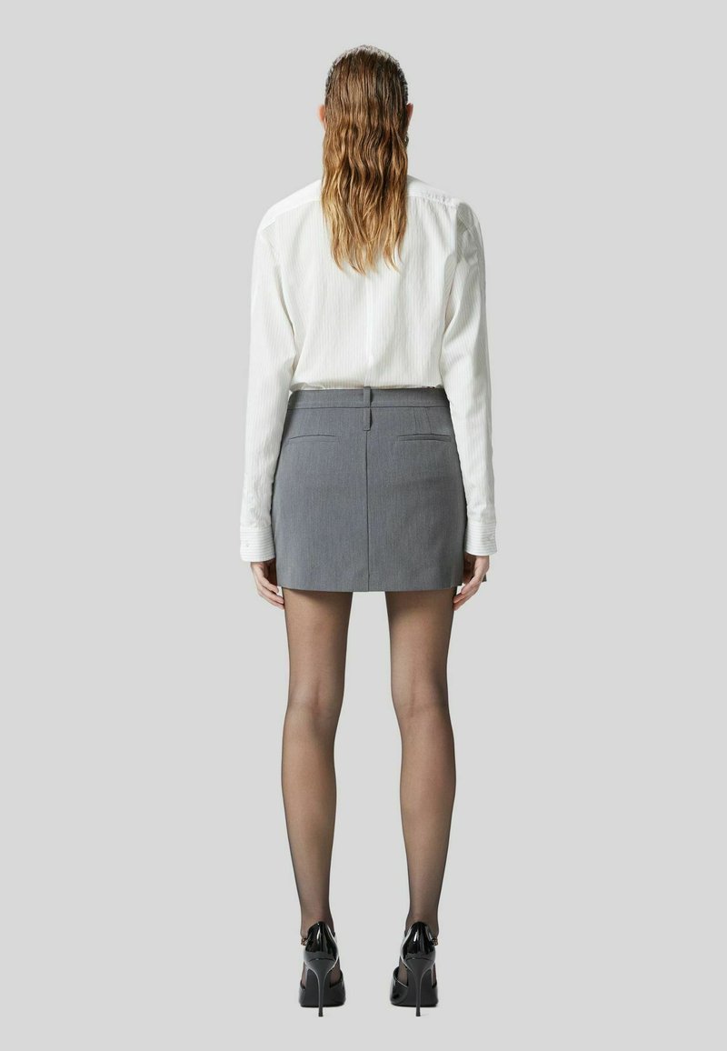 Grijze minirok met een op maat gemaakt ontwerp, gecombineerd met een witte blouse met lange mouwen, zwarte hoge hakken en doorschijnende panty's.