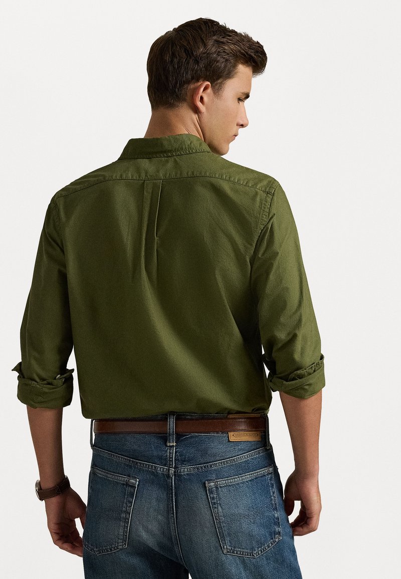 Green cotton shirt with rolled sleeves and back pleat, paired with blue denim jeans, showing a brown leather belt.